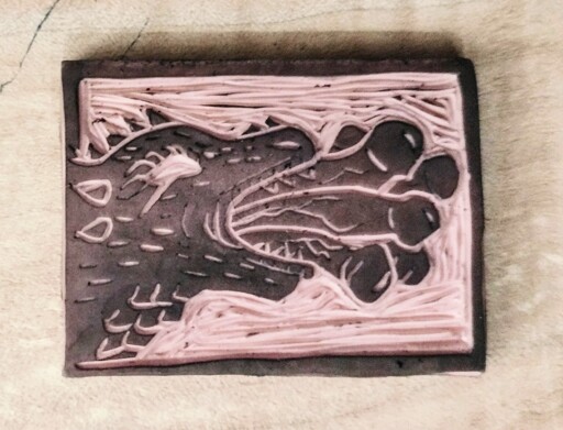 A 5cm wide rectangular pink linocut stamp of a medieval style dragon head breathing a flurry of penises instead of fire.